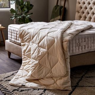 A cream duvet draped over a mattress on a bedframe with an upholstered headboard