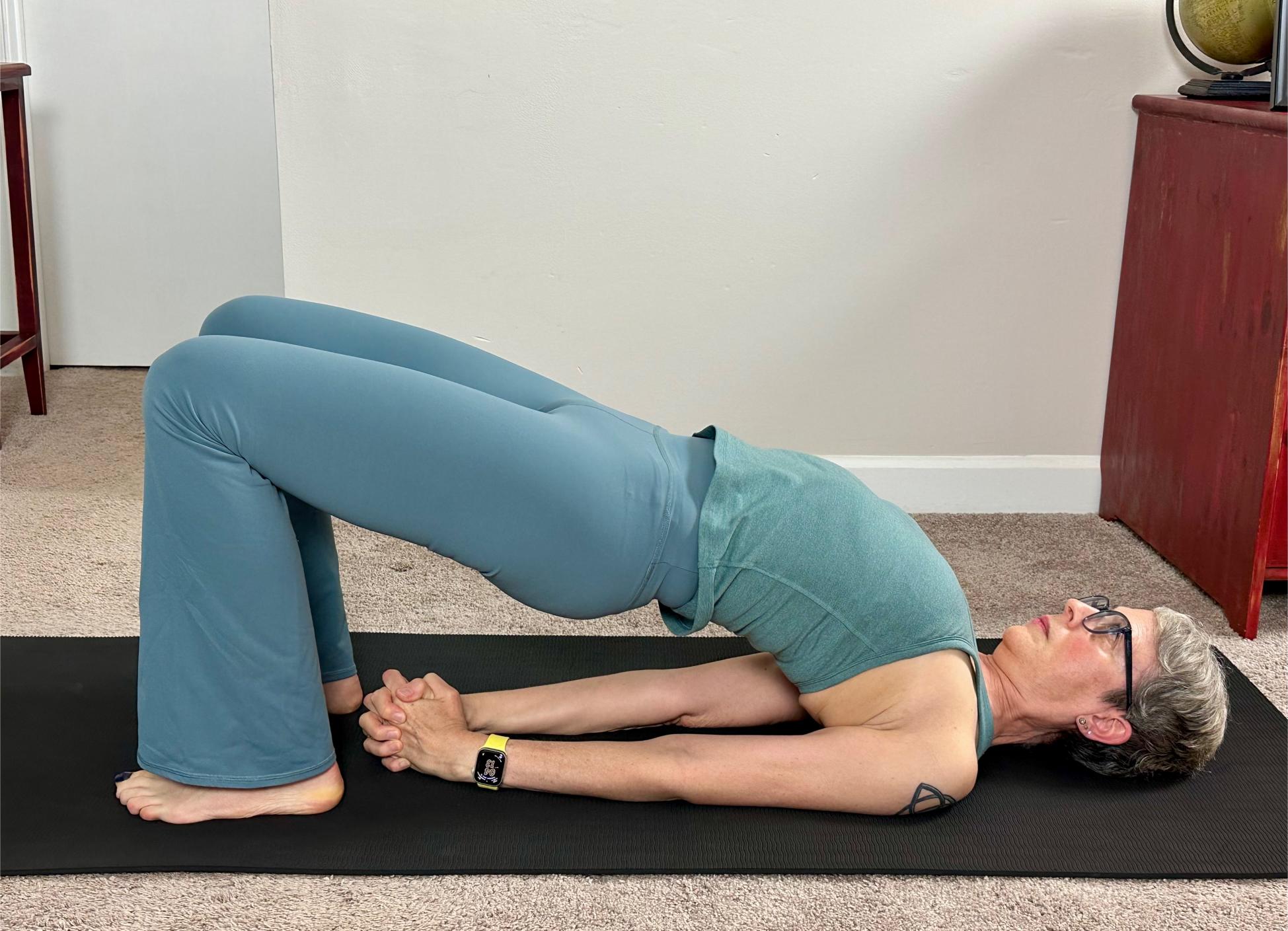 woman performing bridge pose on a black yoga mat in a living room