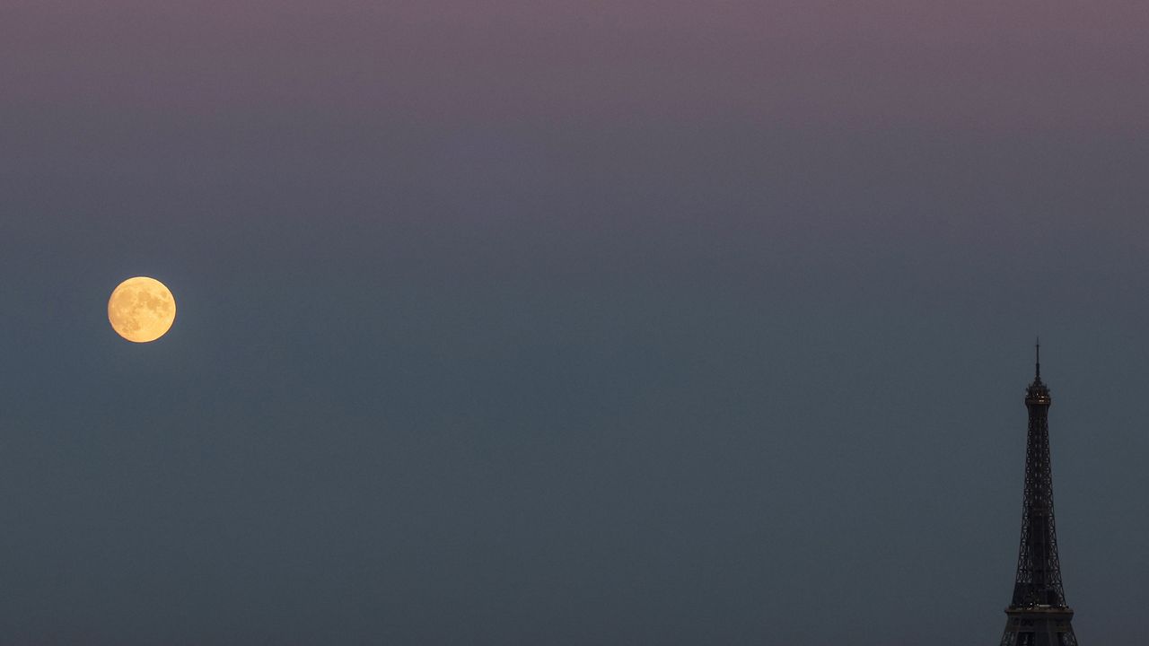 The full moon rises on the side of the Eiffel Tower in Paris, on October 8, 2022.