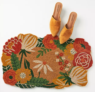 A floral doormat pictured on a white background with a pair of mustard shoes.