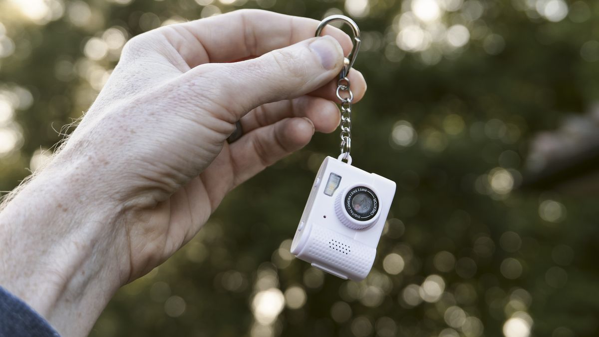 Miniature pink keychain camera, the 'Photo Creator Mini Digital Camera series 3', in user's hand, dangling from keychain