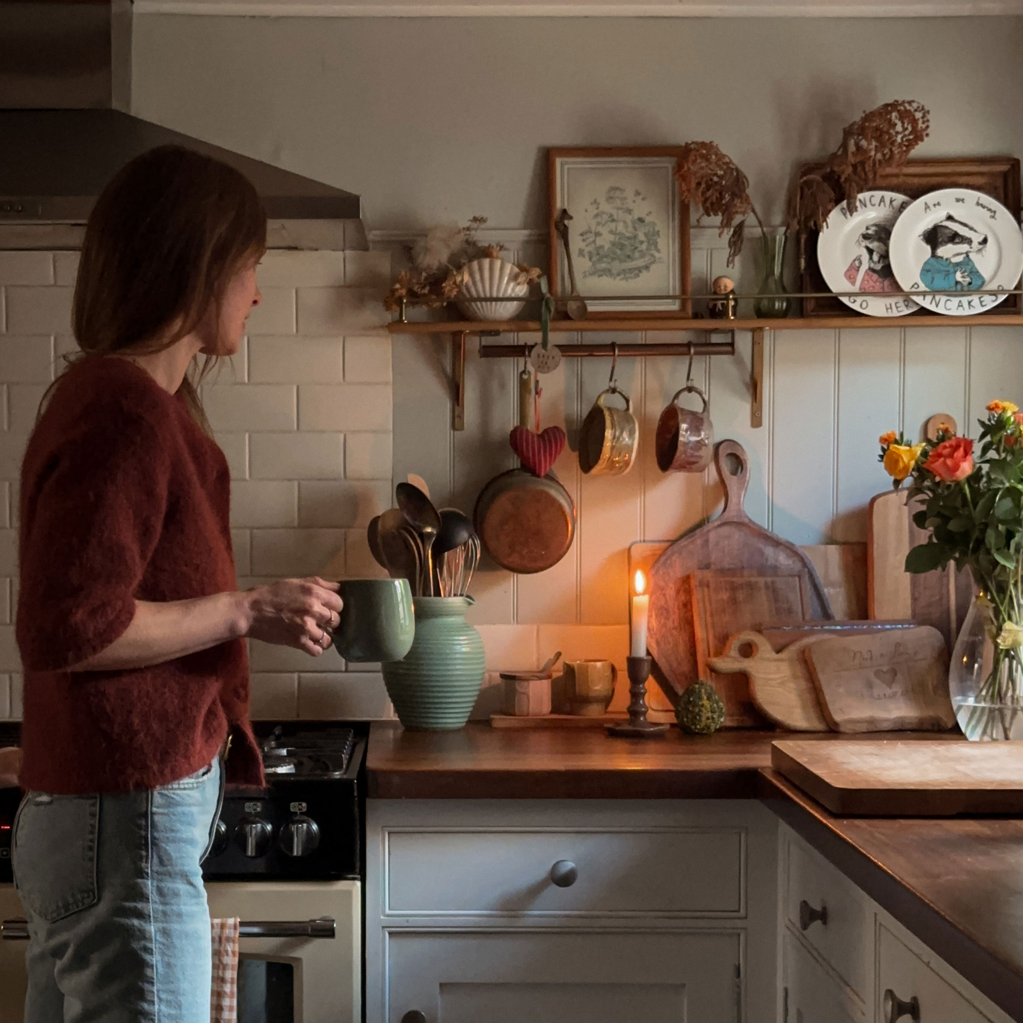 Woman holding mug in kitchen with candle burning