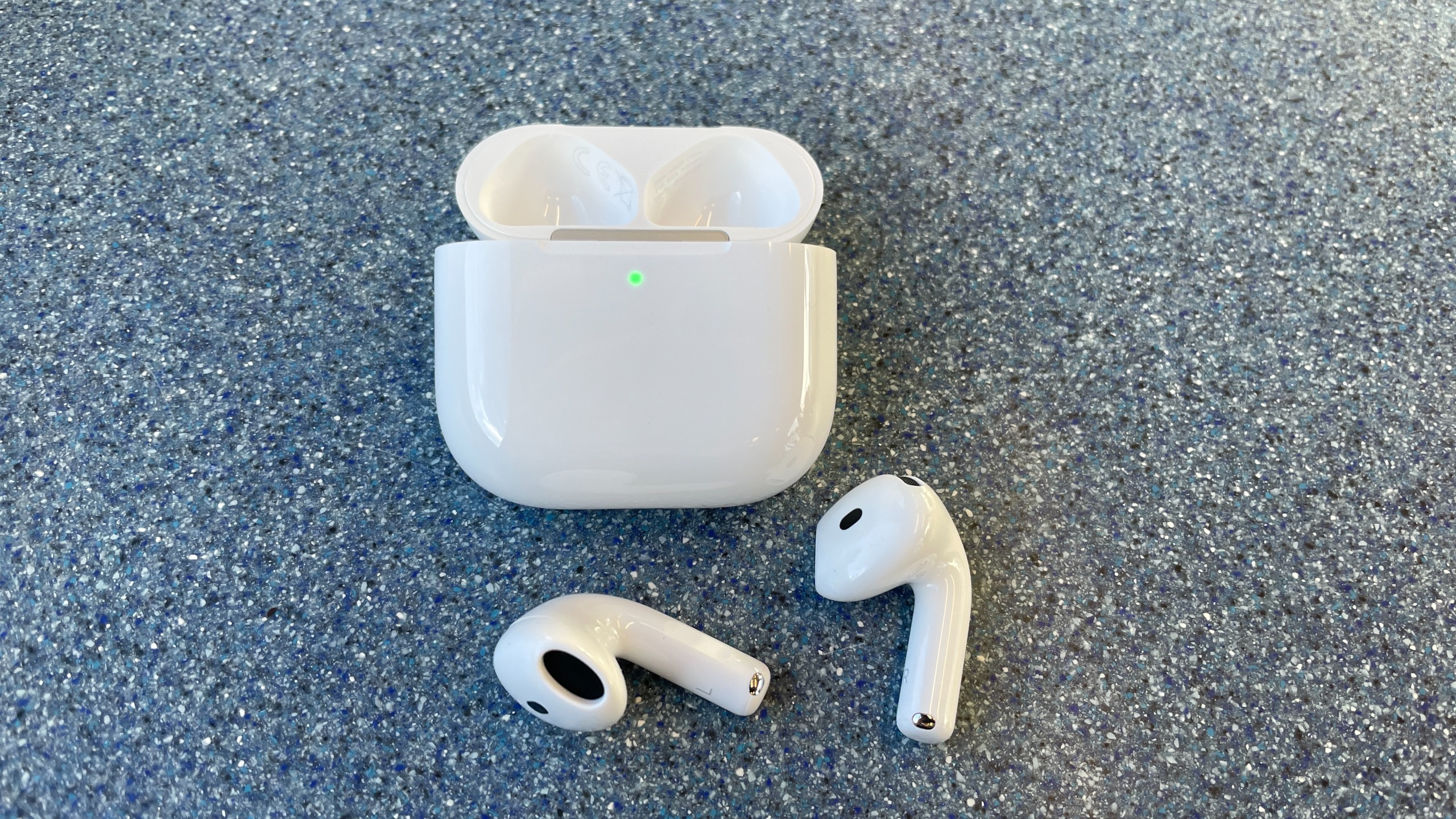 Apple AirPods 5 with Wireless Charging, on a blue table