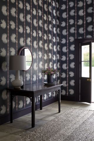 purple entryway way with wallpaper, side table, stone floor, rug, lamp, plant, mirror