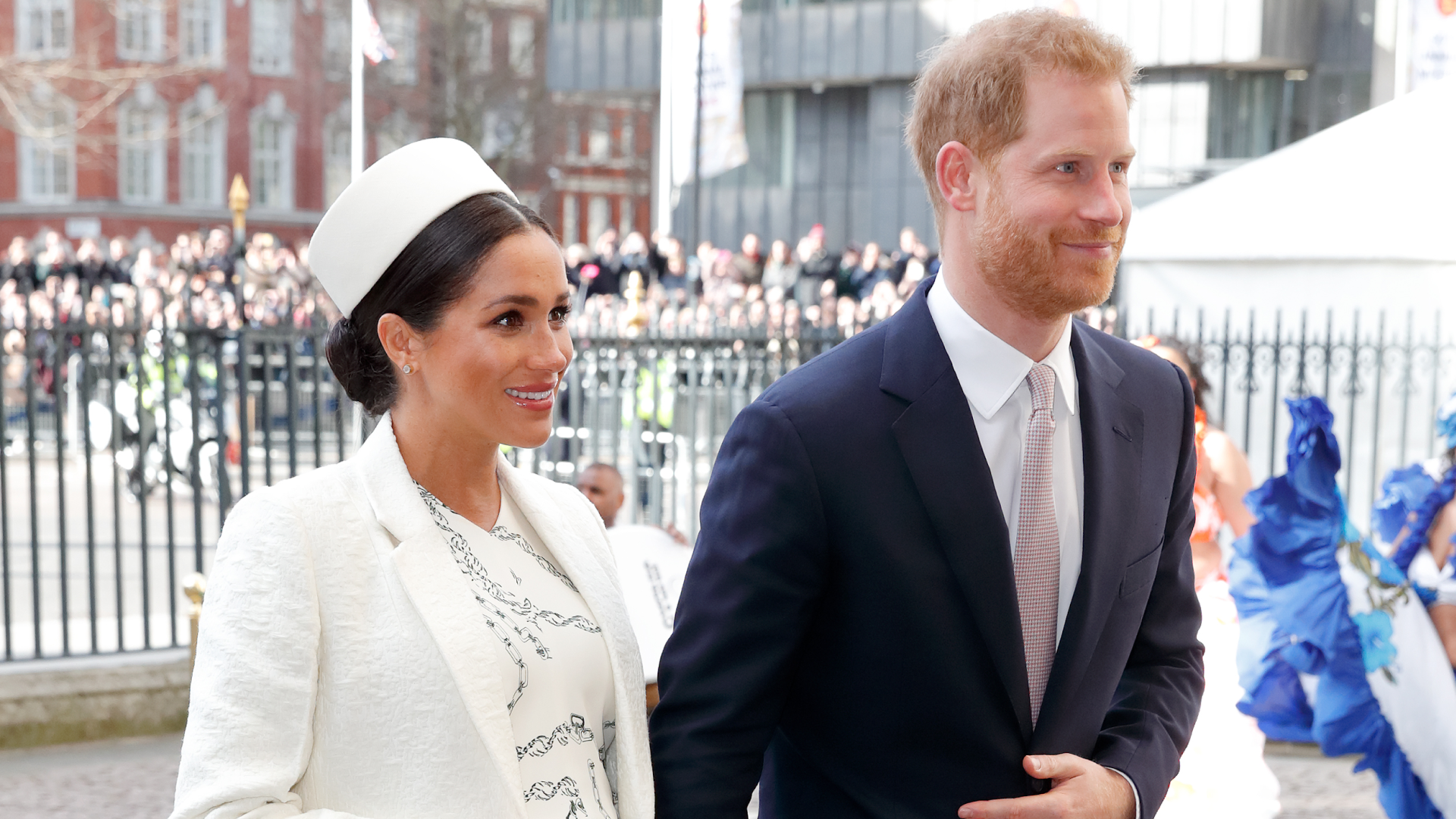 Meghan Markle wearing a white hat and coat holding hands with Prince Harry at Westminster abbey