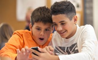 Two boys smile while looking at a cell phone