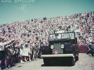 Queen Elizabeth and Prince Philip in an open-topped car driving through a massive crowd of fans