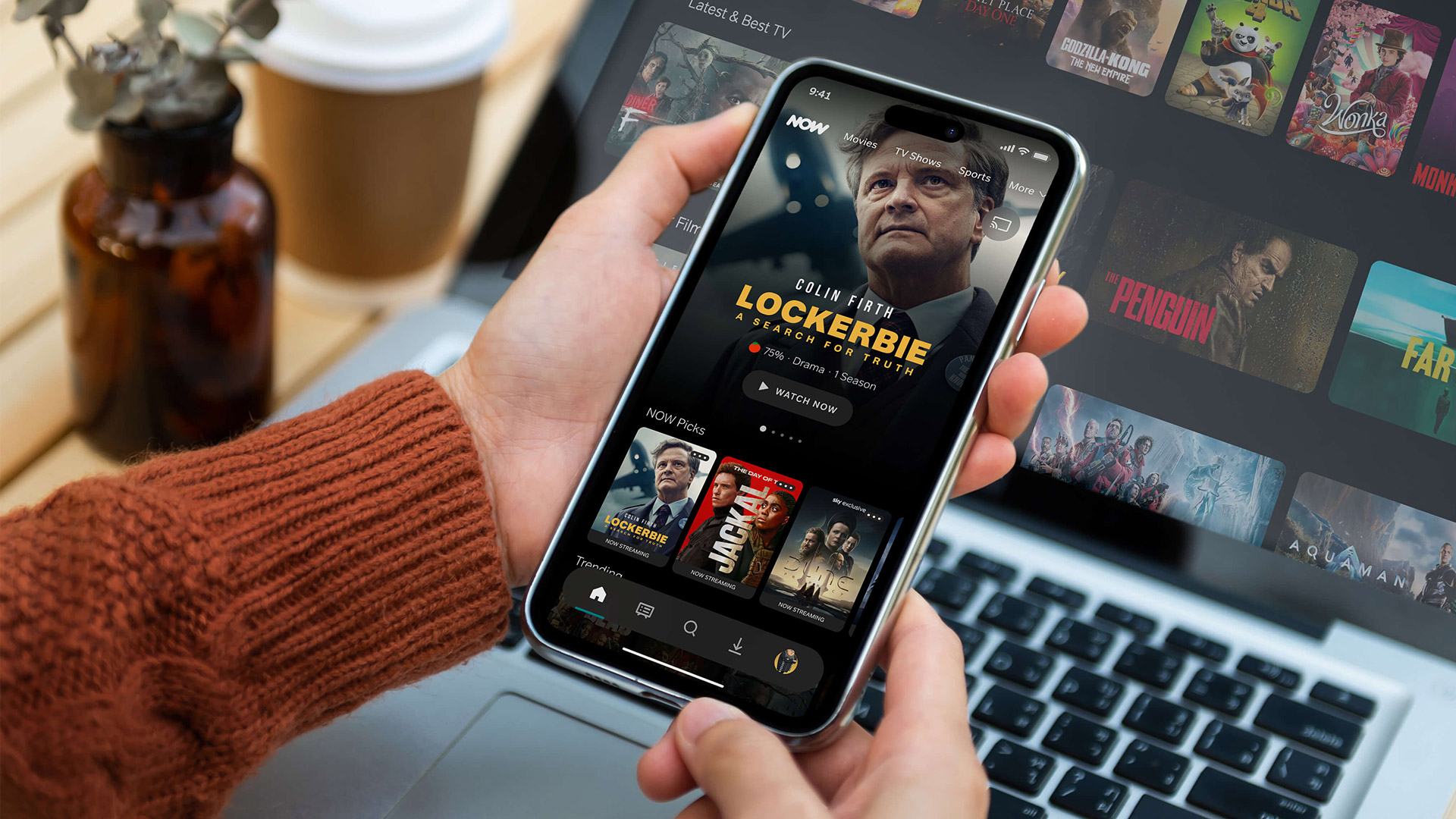 A hand holds a phone showing the Now app 