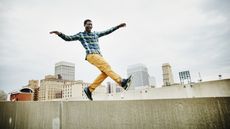 A man dances on the wall of a rooftop with a city skyline in the background.