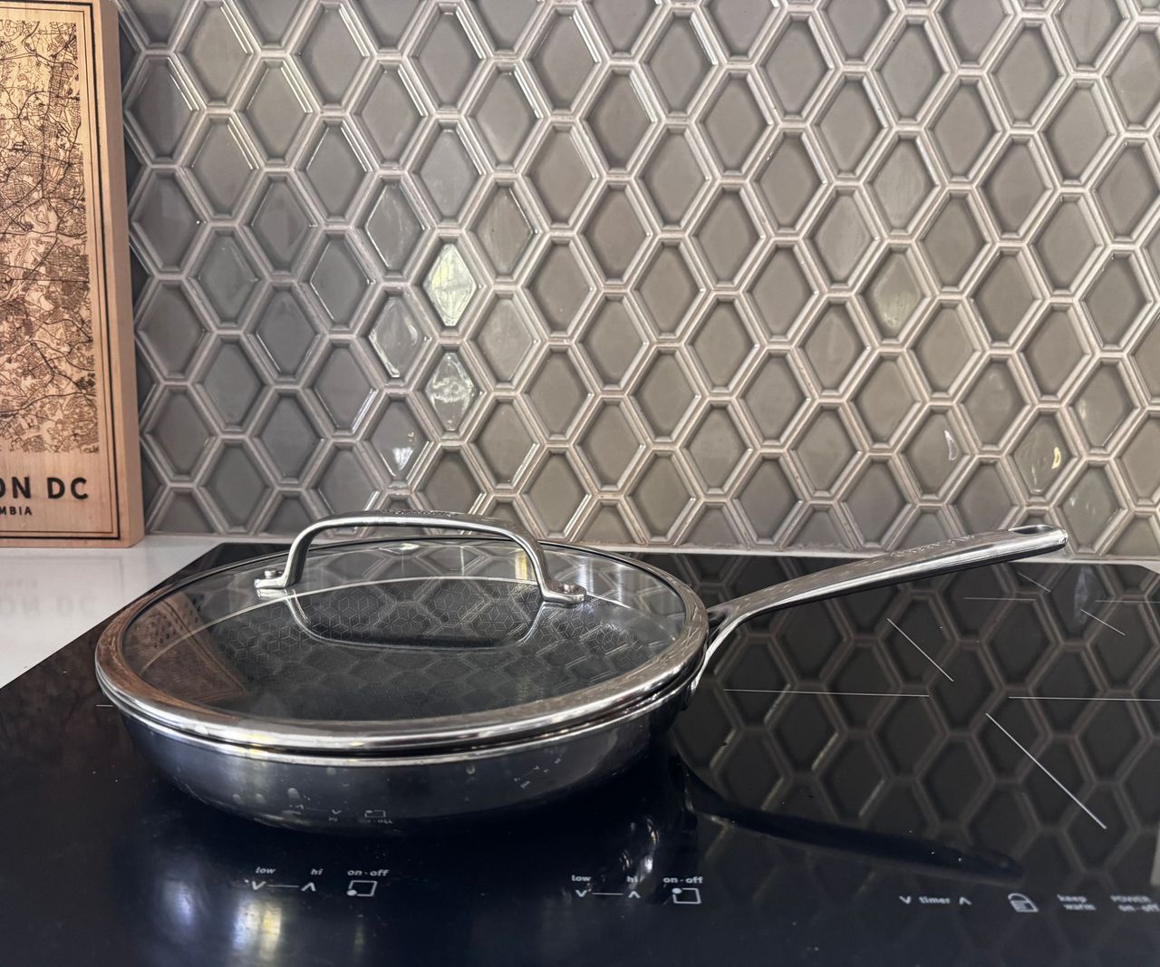 A small stainless steel frying pan with a glass lid on a black induction worktop.