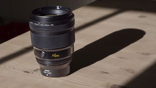Nikon Z 135mm f/1.8 S Plena lens in sunglight on a wooden table with long shadow
