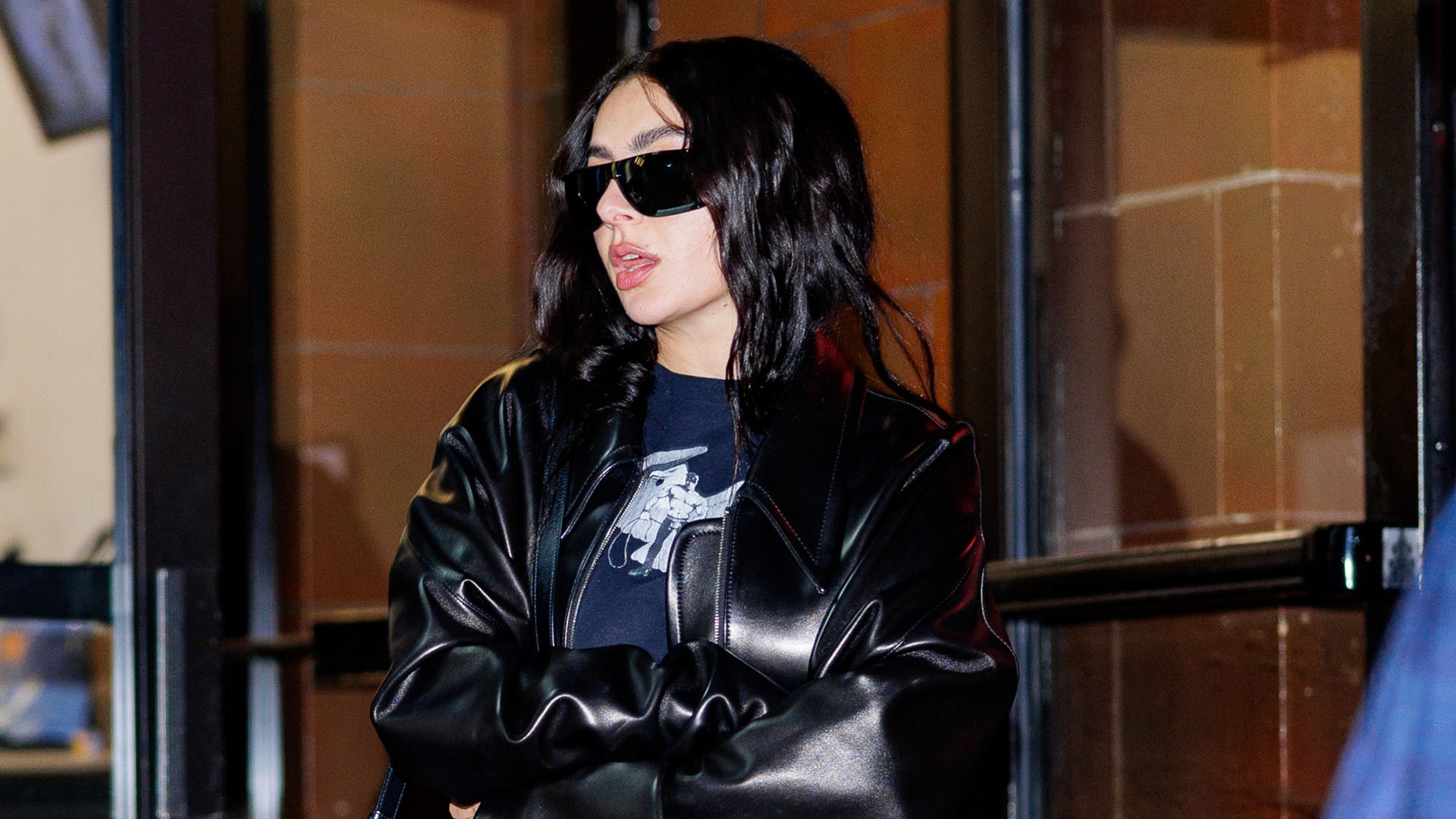 Charlie xcx wearing a black leather jacket, blue jeans, and black boots