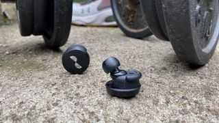 NuraTrue workout earbuds in front of some dumbbells