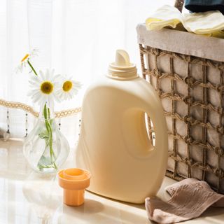 Laundry detergent bottle next to a basket of dirty clothes and a flower in a vase