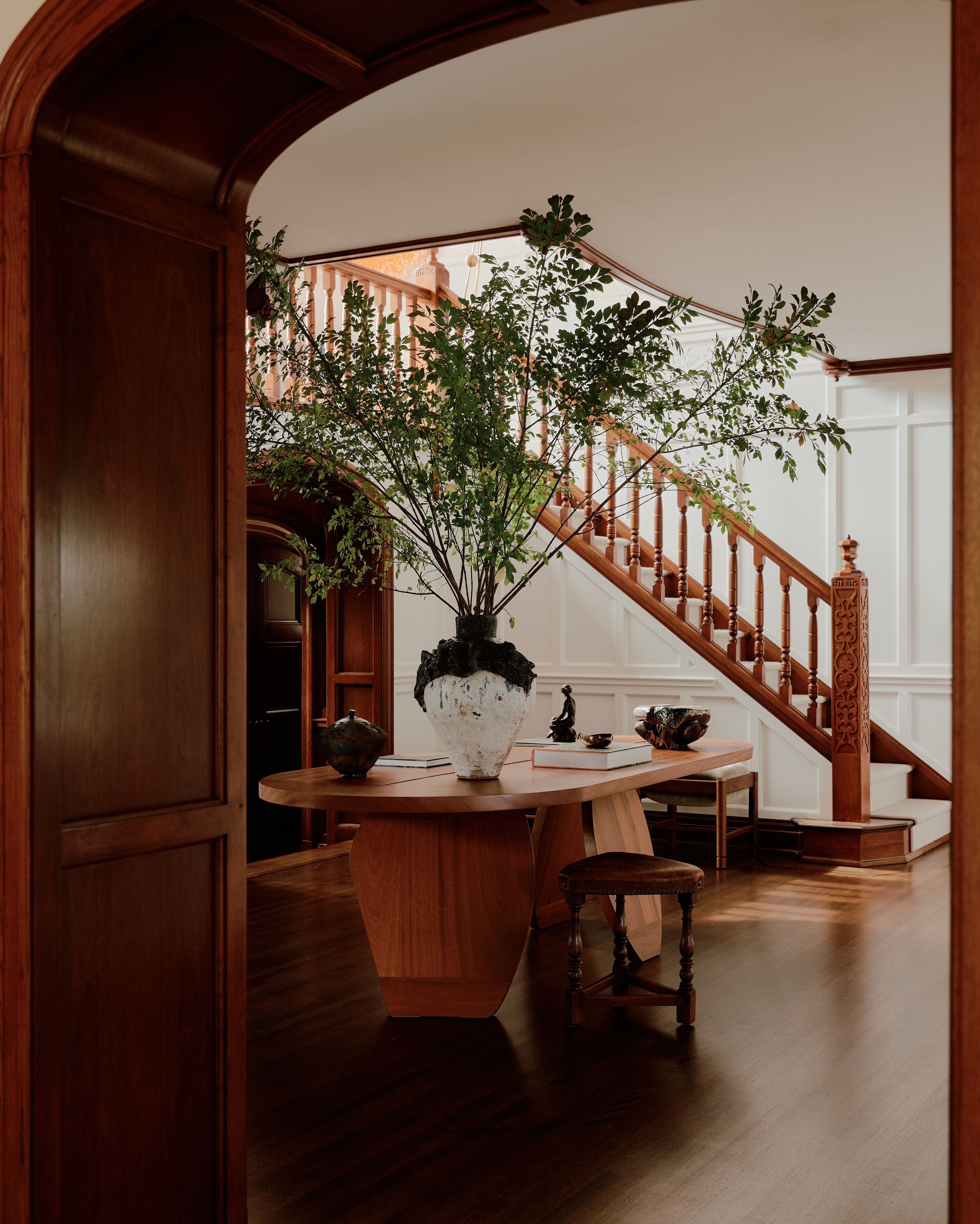 Interior of a Tudor home with sleek wood floors and paneled walls, thriving plants, and sculptural decor.