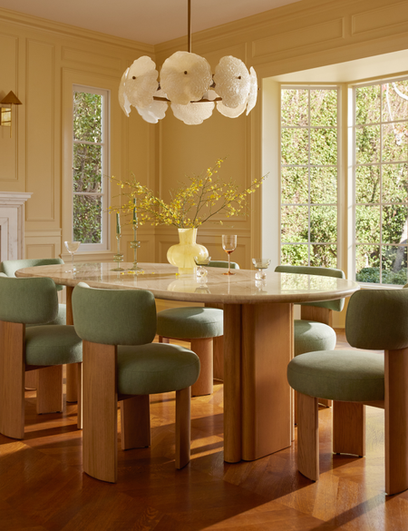 Cheerful butter yellow dining room styled with sculptural mid-century-style dining furniture and a floral-inspired chandelier overhead