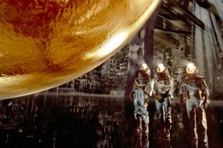 Still from the film "Sphere" showing three scientists beside a golden orb inside a spacecraft.