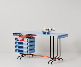 Desk formed from black and red metal tubing and blue, curved top and shelving