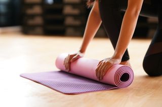 Young woman folding yoga mat after class end