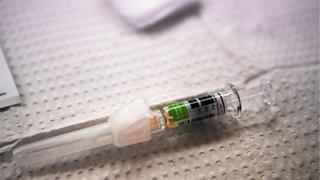 Close-up of a flu shot lying on what appears to be a white piece of fabric with tiny squares on it. The background is slightly blurry.