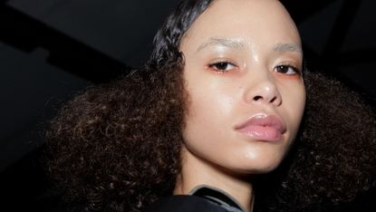 A cropped image of a model with dewy skin and orange eyeshadow under her eyes.