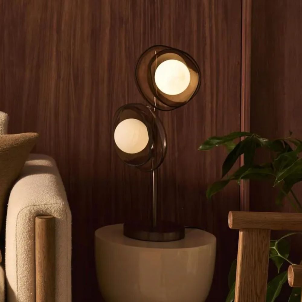 A warm, modern corner featuring a sculptural table lamp with two glowing orb bulbs encased in smoked glass shades