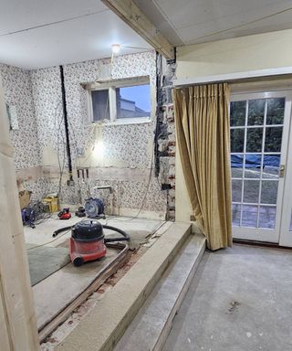 room mid-renovation with wall knocked down, yellow curtains and red vacuum cleaner