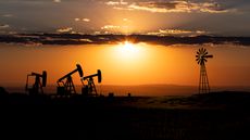 Oil rigs and a nearby windmill at sunset.
