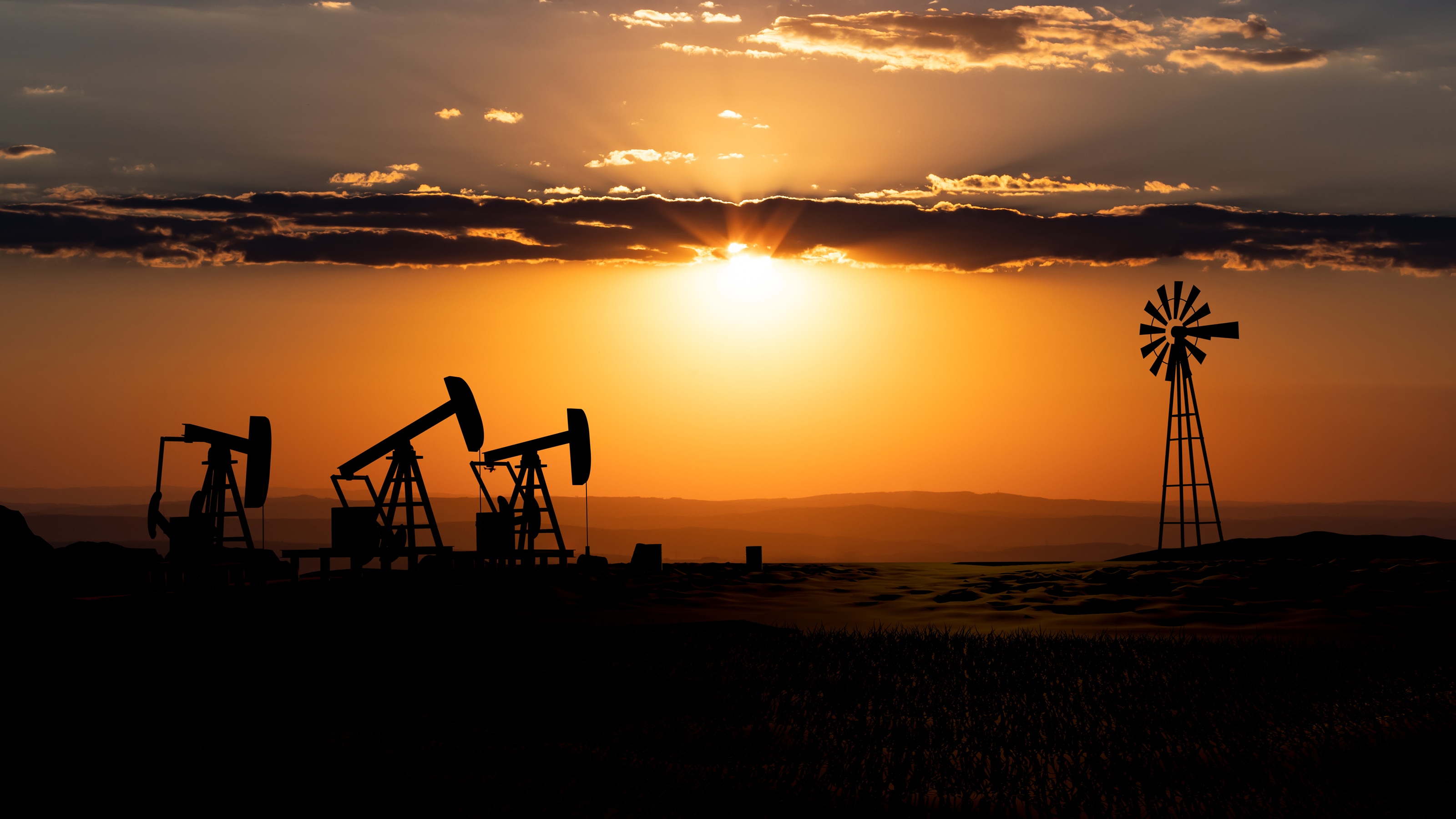 Oil rigs and a nearby windmill at sunset.