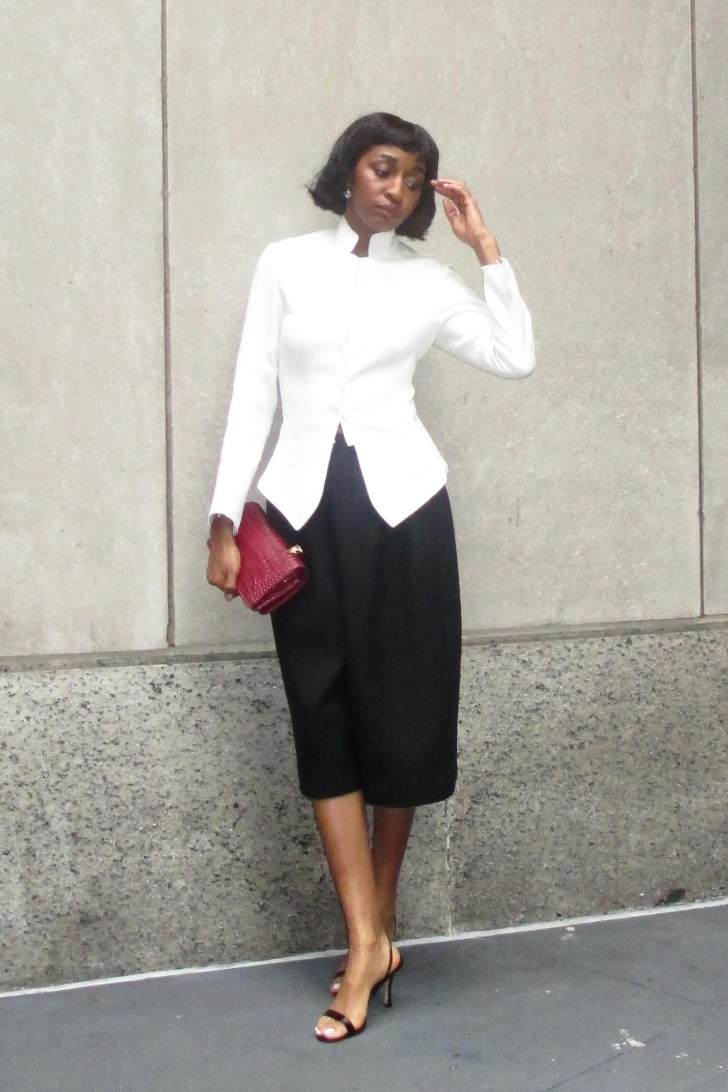 a woman wearing a white button down, black long shorts, and black heels