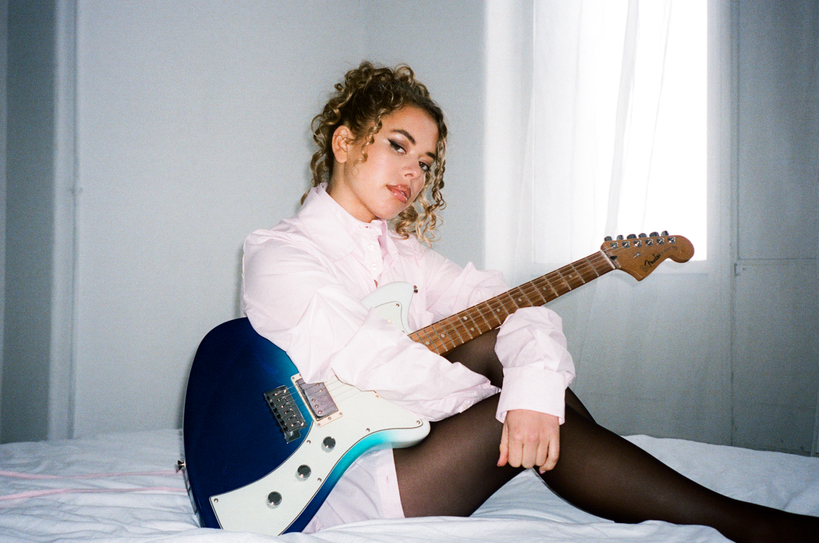 an image of artist Nil&amp;uuml;fer Yanya sitting on a white matress in a bedroom
