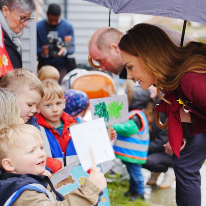 Princess Kate talking to kids bending over holding an umbrella