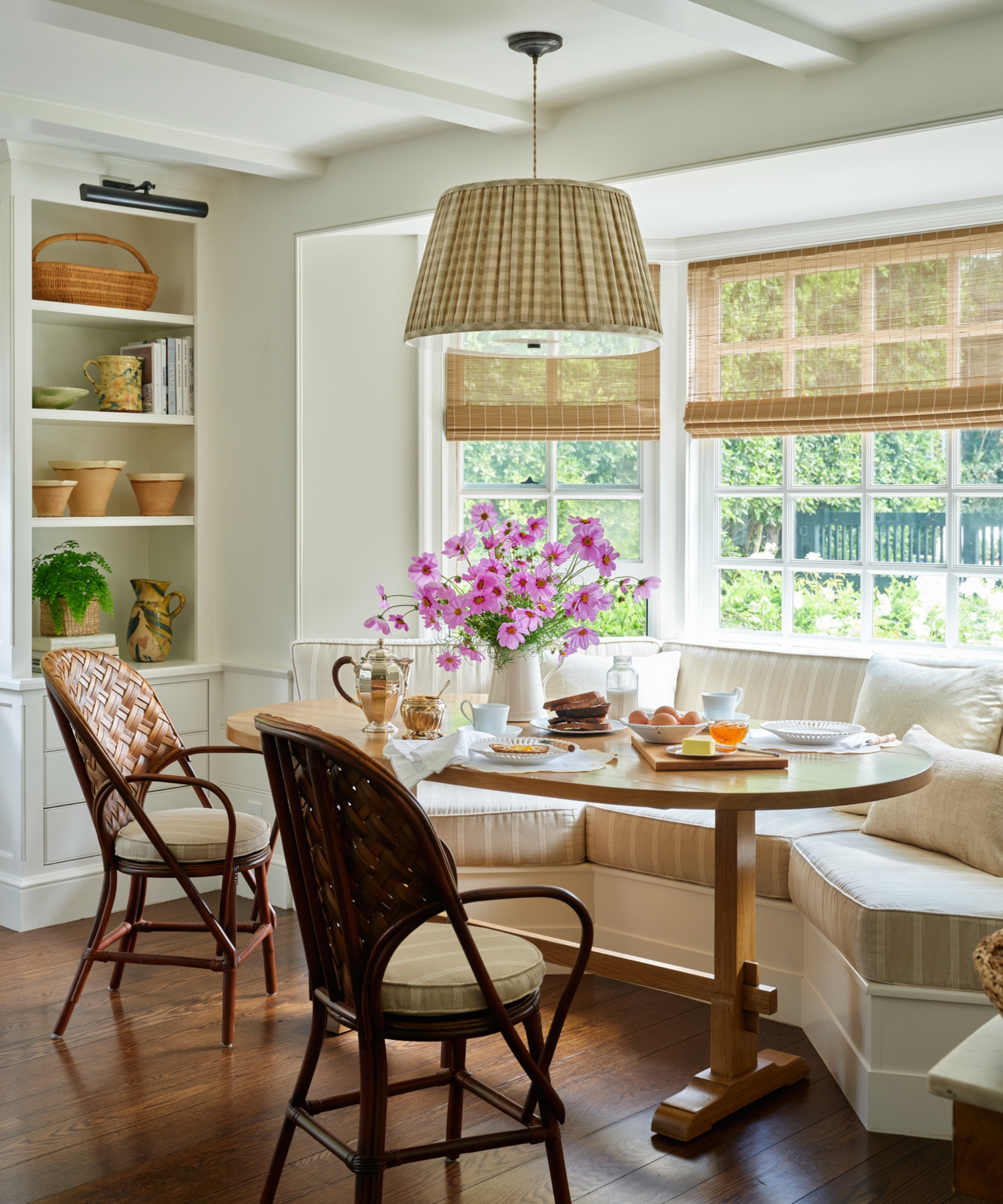 A large kitchen banquette in a bay window, featuring beige and white striped seat cushions and a wooden table