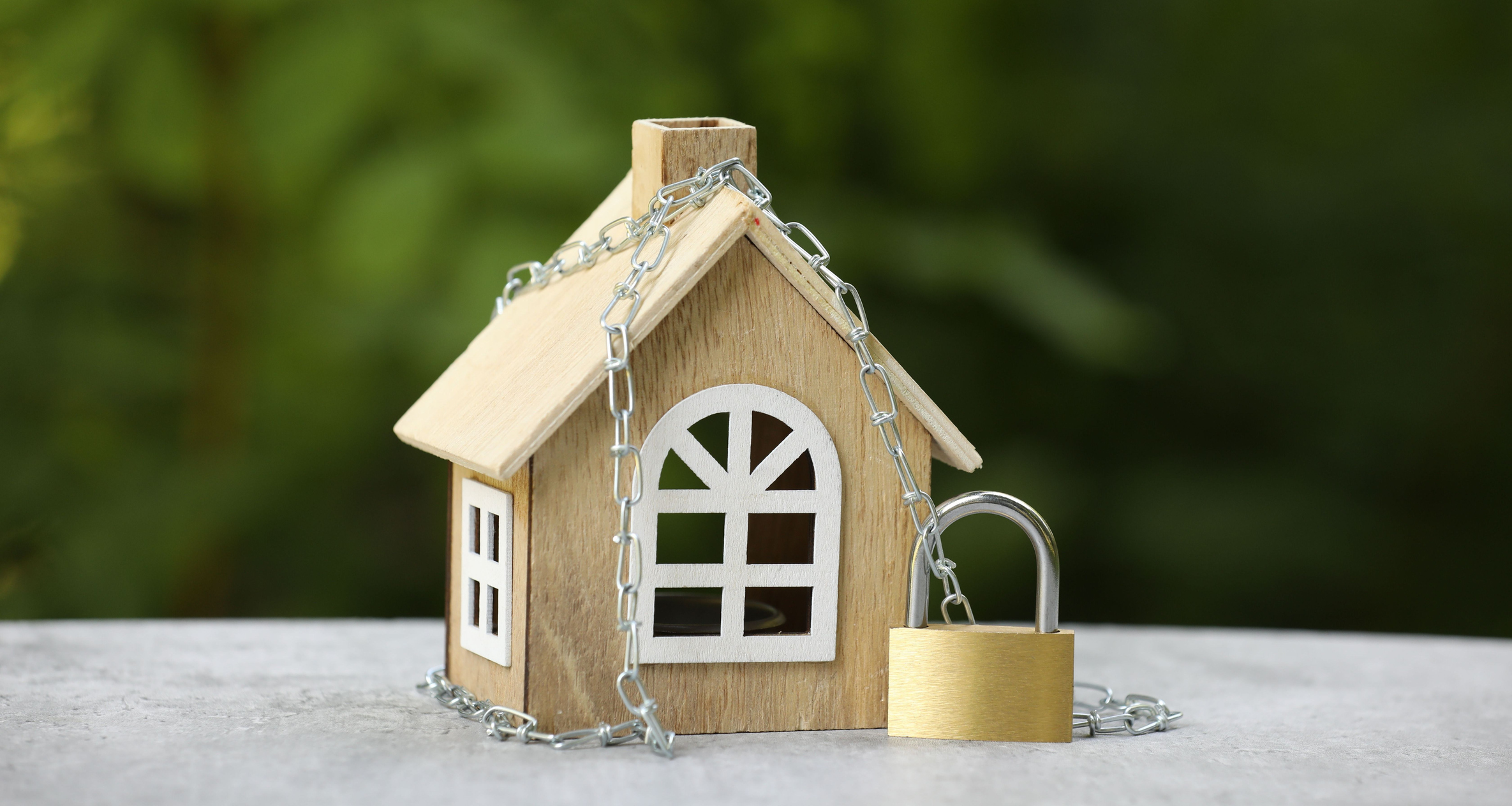 House model, chain and padlock on light grey table outdoors, closeup