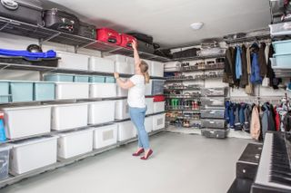 Garage with fitted shelving and racks and woman reaching up to access suitcase