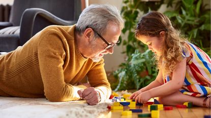 A grandfather and his granddaughter play a game together on the living room floor.