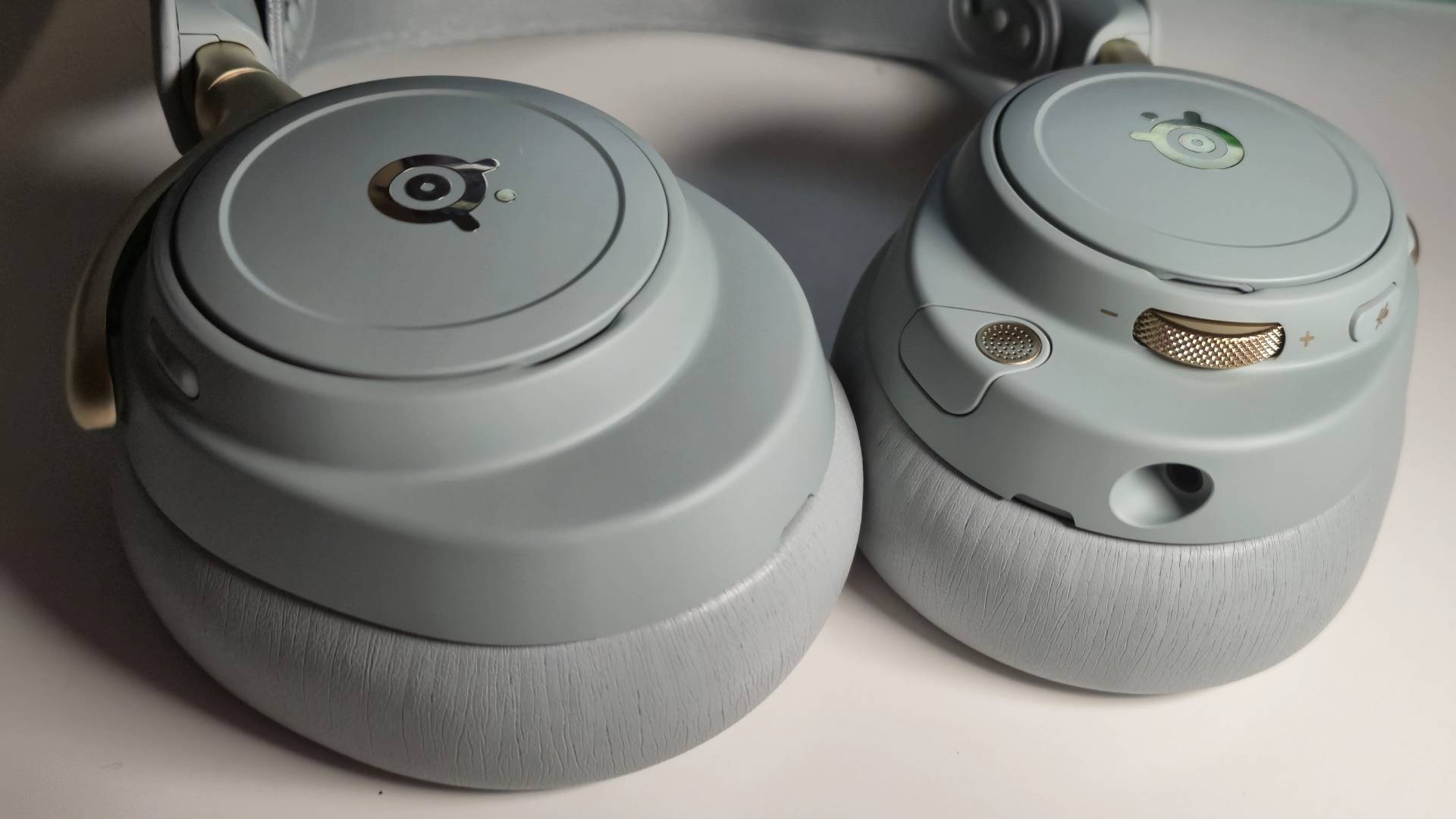 Photo showing the edge of the earcups of the SteelSeries Arctis Nova Elite headset in Sage Gold sitting on a white desk.