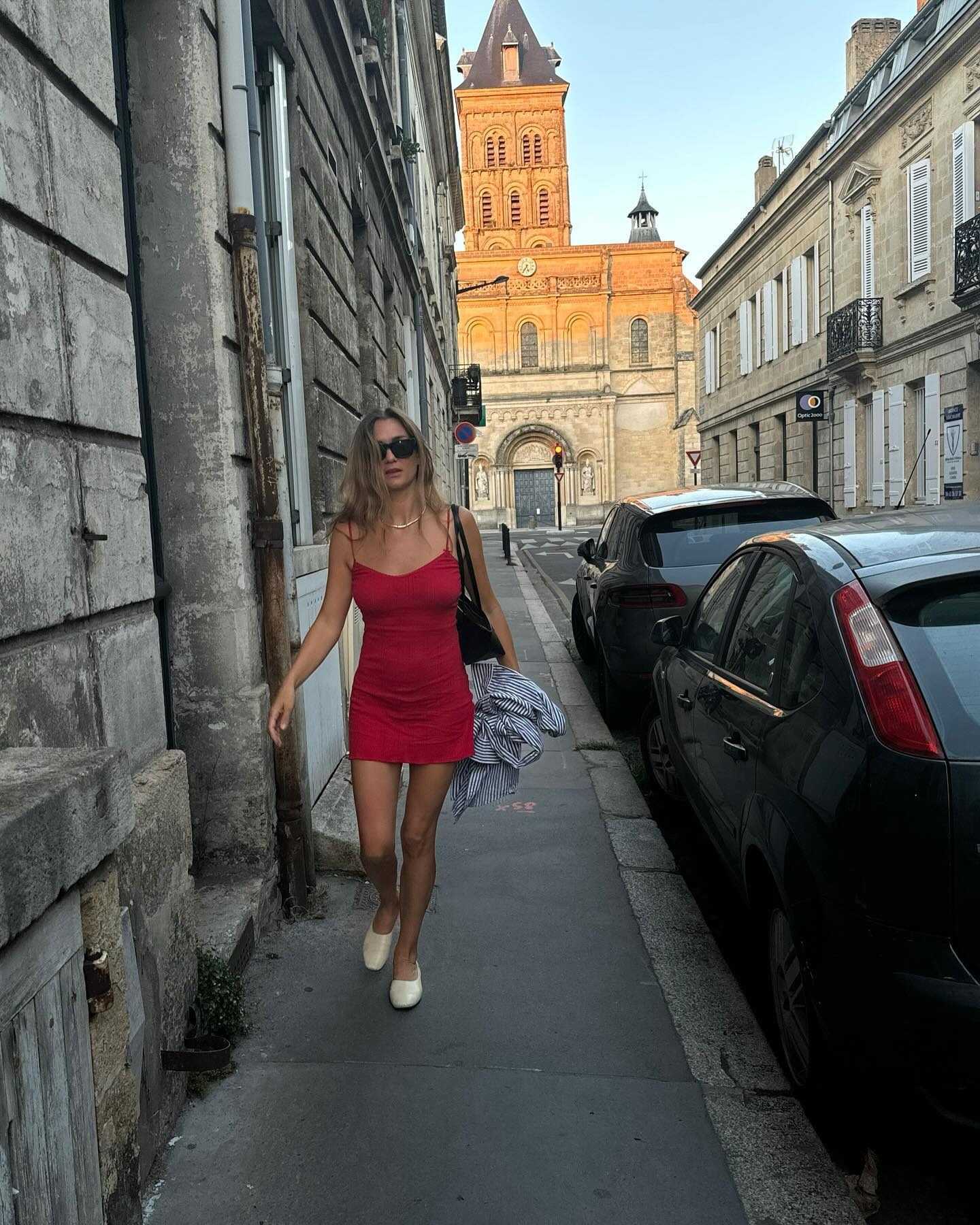 Influencer @annelauremais walks outside wearing a red minidress with cream ballet pumps in Paris.