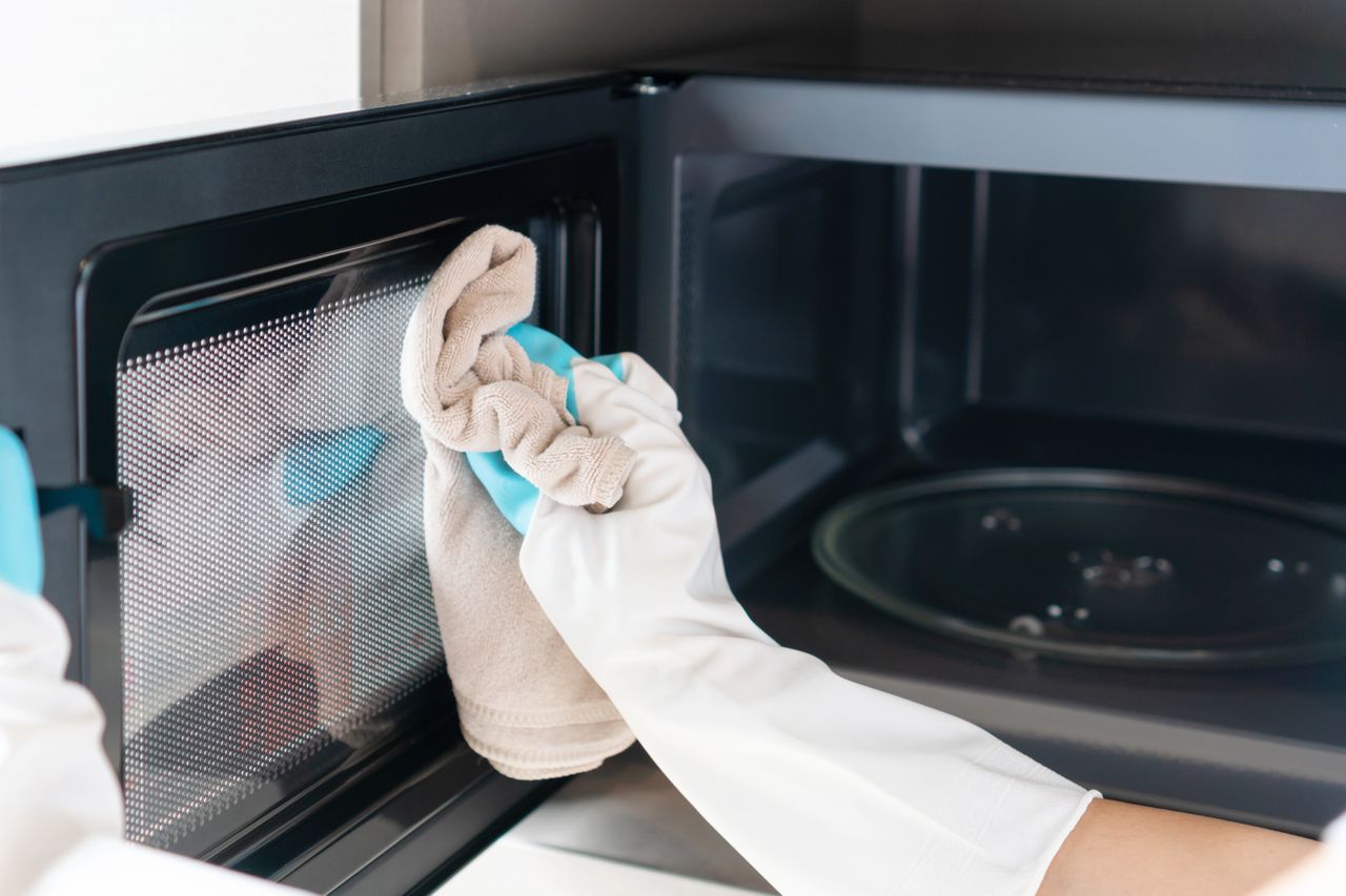 A person using a cloth to clean a microwave door. 