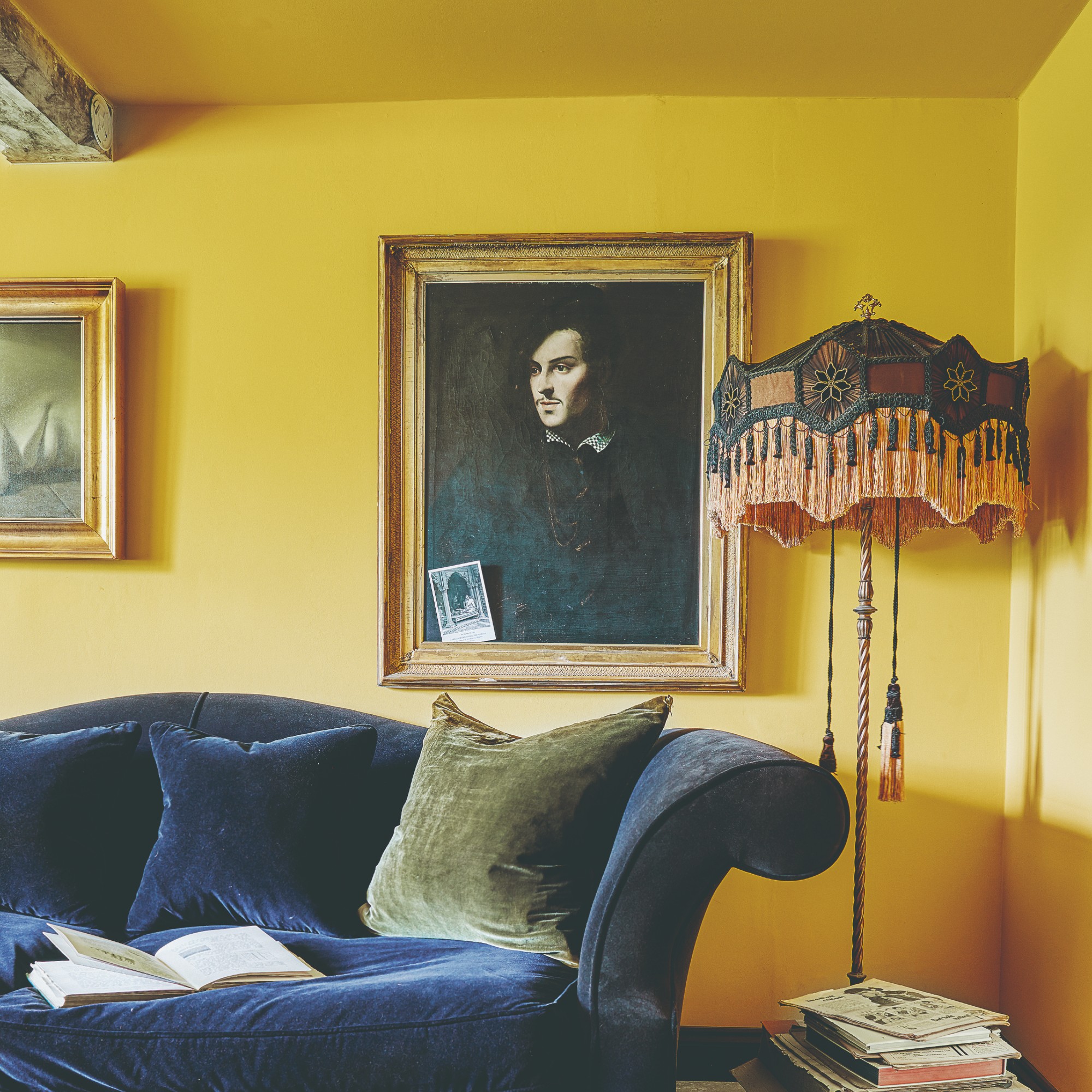 A sunny yellow-painted living room with a sheen on the walls and a curved blue velvet sofa