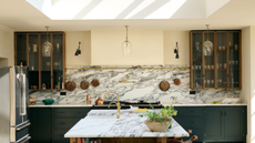 glass fronted cabinets in a marble clad kitchen with dark teal cabinetry