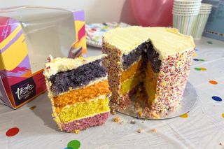 Sainsbury’s Rainbow Layer Cake Taste the Difference being cut to reveal rainbow sponge layers