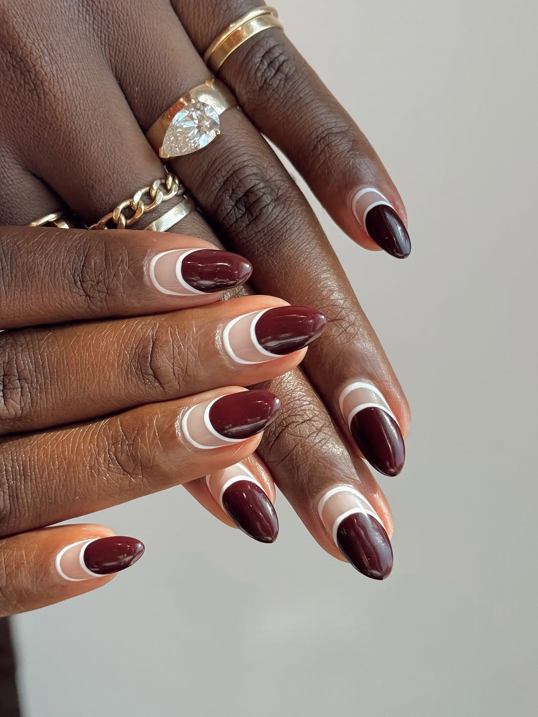 Close-up photo of a person&amp;rsquo;s hand showcasing a maroon and white oval manicure on almond nails.