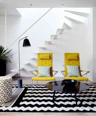 A white living room picture with yellow chairs and monochrome patterned rug.