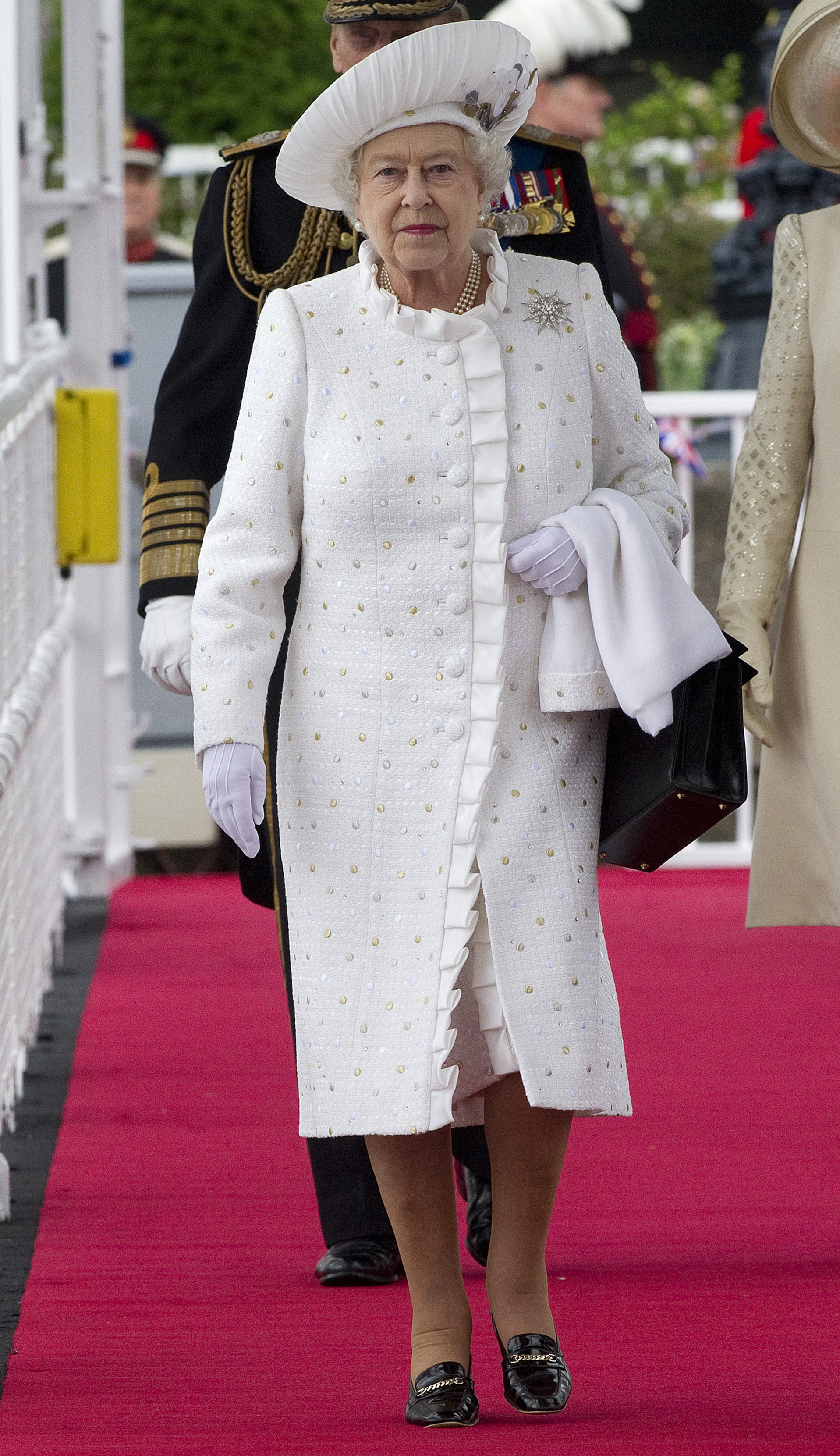 Queen Elizabeth wearing white coat and hat walking down a red carpet
