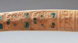 The bone is delicately carved with designs that represent a catfish and inlaid with pieces of turquoise.