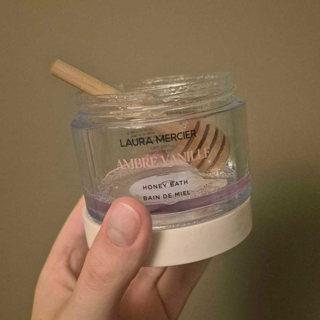 Hand holding empty tub of Laura Mercier Honey Bath Ambre Vanille