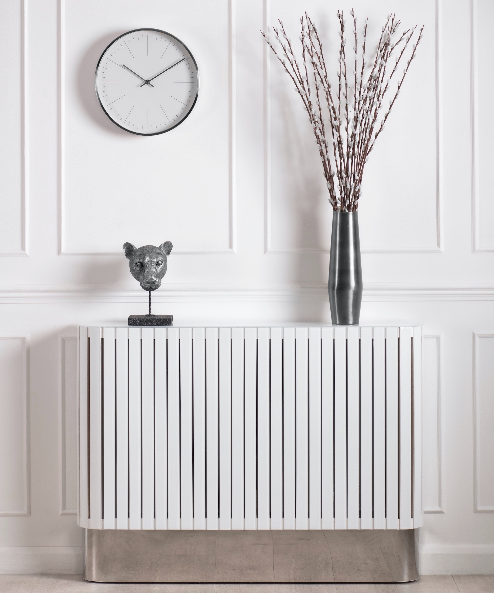 White radiator cover against white wall panels with a silver base and silver ornaments on top