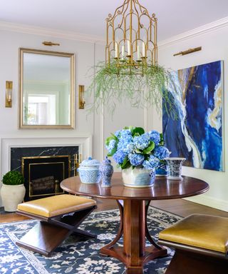 neutral hall with round wooden table, black fireplace, leather stools, blue statement artwork and blue patterned rug