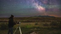 a man stands shining a laser to messier 7 which is in the tail of the scorpius constellation.